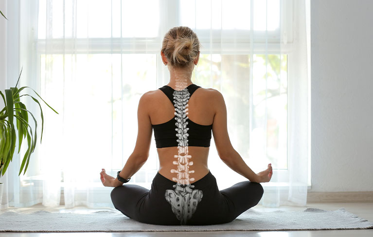 Rückenschonend durch den Alltag Frau sitzt im Schneidersitz vor einem hellen, großen Fenster